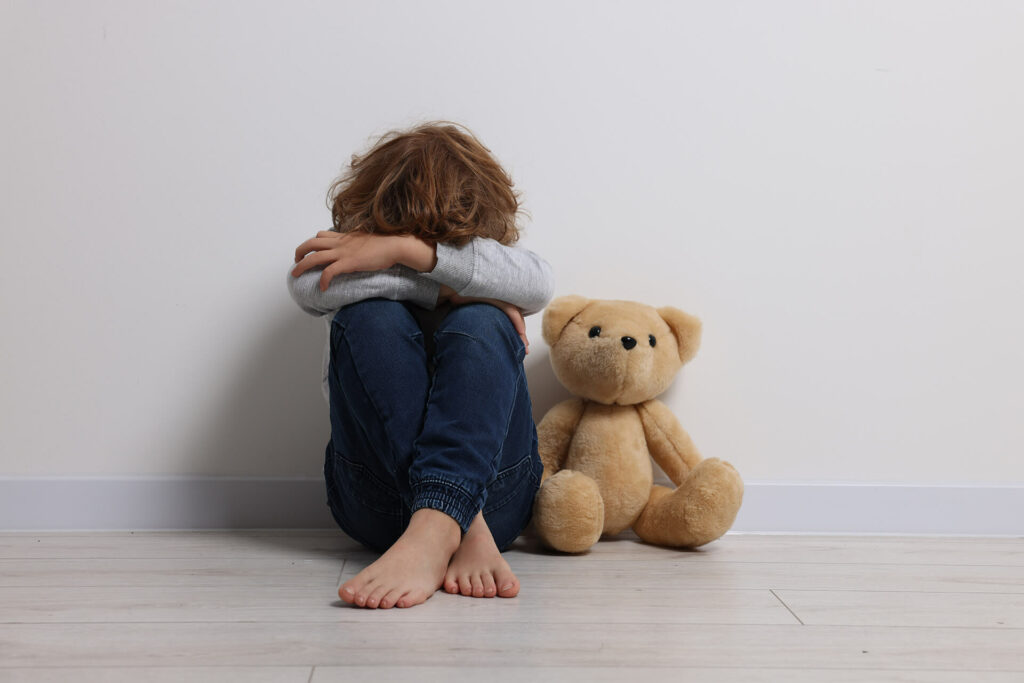 Enfant assis tete dans ses bras avec nounours à côté